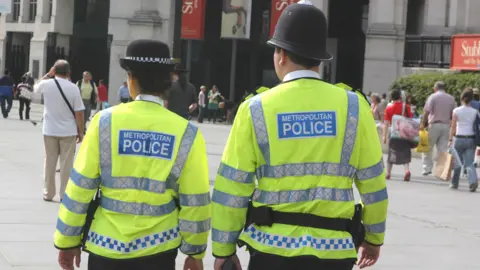 Two police officers on patrol in London. They have their backs to the camera and are wearing high vis jackets.