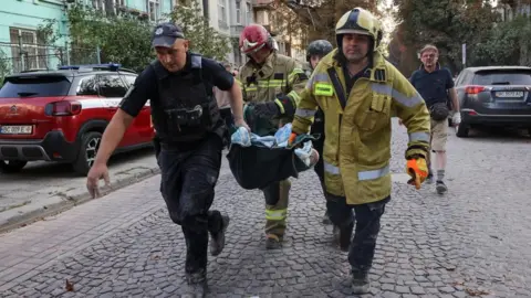     REUTERS/Roman Baluk Een politieagent en hulpverleners vervoeren een gewonde persoon die is gered uit een woongebouw dat beschadigd was tijdens een Russische drone- en raketaanval, te midden van de Russische aanval.