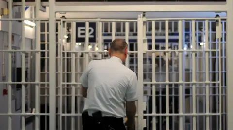 PA Media Male prison guard locks a white internal prison door. His back is to the camera.