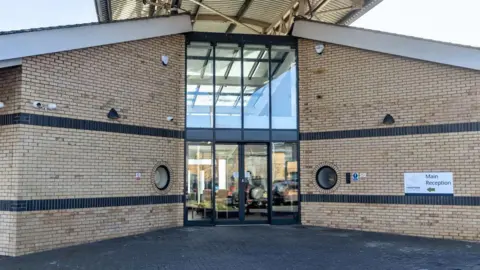 Front entrance of Hamptons Hospital, it is a yellow-brick building with glass-fronted entrance doors.