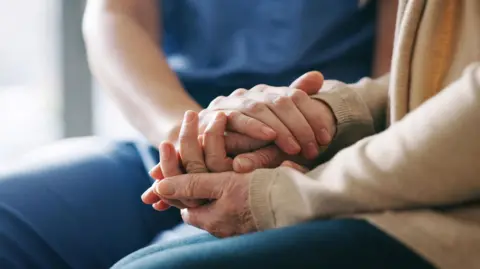 A stock photo of a close up of two people holding hands in a supportive way. 
