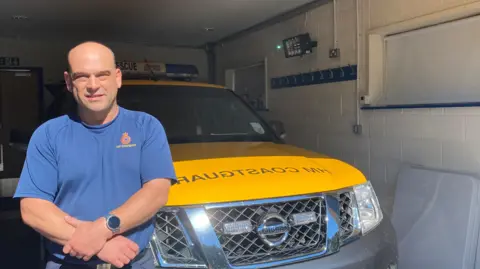 Ian Woods standing in front of a truck marked HM Coastguard 