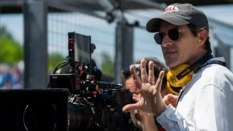 PA Media Director Joseph Kosinski on set standing by a camera wearing a hat and sunglasses