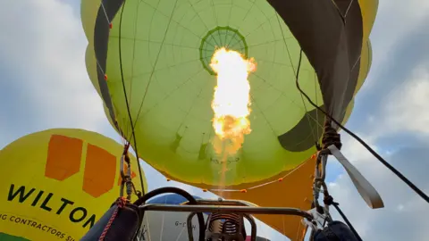 The inside of an inflated hot air balloon. A flame is centre. The balloon is green in colour.