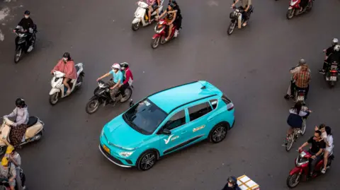 Getty Images A blue VinFast electric car on the streets of Hanoi surrounded by mopeds.