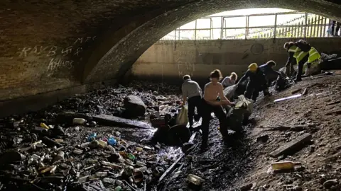 River Roding Trust People are in a dark tunnel picking up rubbish