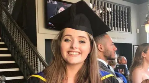 Grace Millane, a woman with brown hair wearing a graduation gown and mortar board.