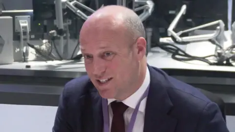 Dan Thomas sitting in a radio studio in front of a microphone, which has an orange cover.