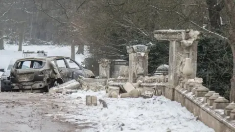 National Trust A burnt-out car sat next to ruined stonework of a bridge in heavy snow