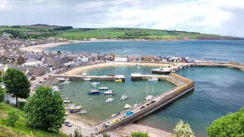 Doug Mackay Stonehaven harbour with boats in water and countryside in the distance.