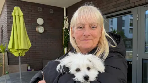 Karen Quinn is pictured in her front garden holding her dog.