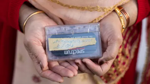 A woman's hands holding a see-through plastic cassette box with a cassette visible inside.