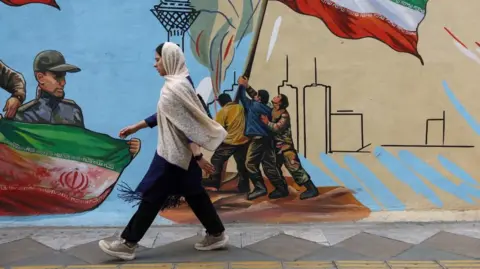An Iranian woman walks next to a mural on a street in Tehran