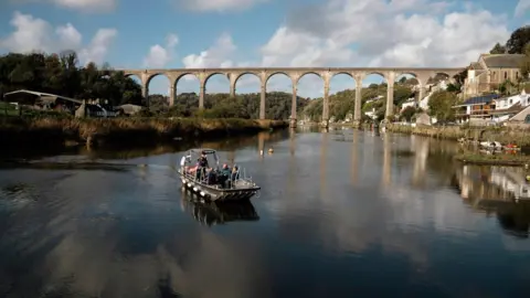 Passengers on the new ferry with the Calstock Viaduct behind them. The sky is blue and cloudy. 