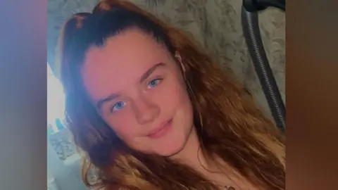 Shannon Hipgrave A woman with long brown hair and blue eyes is smiling