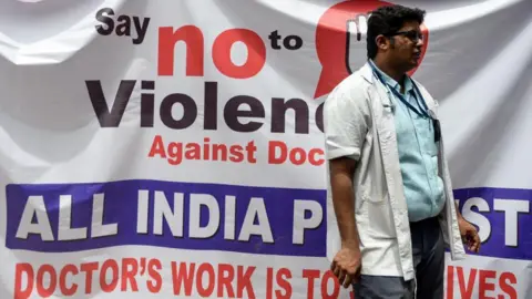 Indian doctors and students stand beside poster as they stage a silent protest during the nationwide doctors strike held after the recent assault in Kolkata on an intern doctor, in Chennai on June 17, 2019. Tens of thousands of Indian doctors went on strike on June 17 calling for more protection against violence by patients and their families, as parliament met for the first time since national elections. (Photo by ARUN SANKAR / AFP) (Photo by ARUN SANKAR/AFP via Getty Images)
