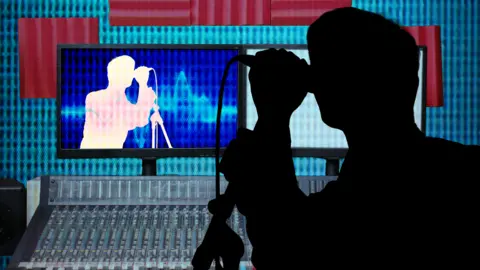 A black shadow of a male is singing into a microphone in a music studio. A music desk sits below a screen projecting the shadow onto a computer screen. 