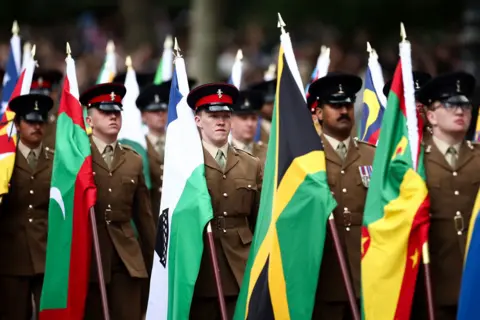 PA Media Members of the military wear uniform and hats as they carry Commonwealth flags and march down the Mall.
