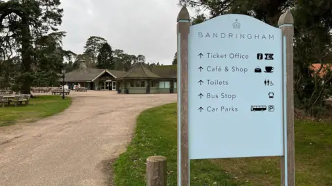 Shaun Whitmore/BBC Gravel driveway to the Sandringham Estate. There is a white sign with details of what is on the estate including ticket office and car parks. The ticket office is in the background at the end of the driveway.