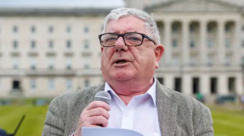 PA Media Gerry Murphy speaking. He has grey hair and is wearing a blazer, white shirt and glasses.
