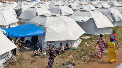 A sea of white tents seen at Rugombo football stadium with people seen outside some of them.