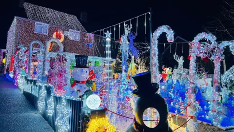 A house with thousands of brightly coloured lights and ornaments. There are Christmas-related ones including a snowman and candy canes. 