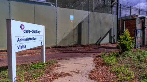 Anadolu  A signpost reads "CARE+CUSTODY" with arrows that show the way to the visiting and administration centre inside the abandoned facility of the Immigration Removal Centre Campsfield in Kidlington near Oxford. Its walls are fenced with barb wire.