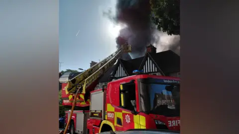 LFB Red fire engine with yellow ladder and black plumes of smoke