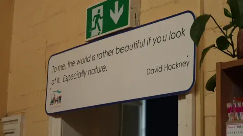 Aisha Iqbal/BBC A large sign above a door which says 'To me, the world is rather beautiful if you look at it. Especially nature'. It is attributed to David Hockney.