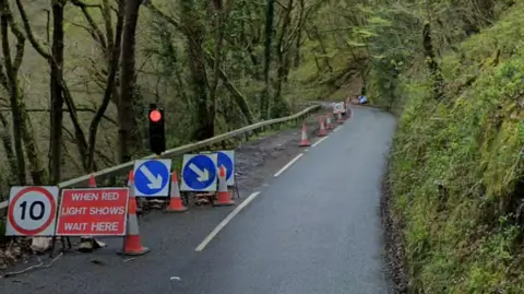 Signage showing a 10mph speed limit and a red traffic light at the start of the lane closure on the B3212 going through woodland between Doccombe and Dunsford
