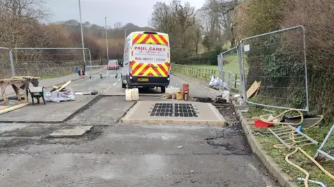 Roadworks including freshly laid concrete and a metal rectangular grid.