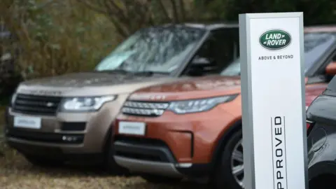 AFP via Getty Images Two range rovers parked next to a sign saying Land Rover