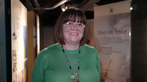 Shaun Whitmore/BBC Natalie Fairweather stands in the museum. The walls have information about shipwrecks and rescues.