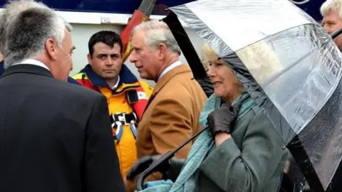 King Charles and Queen Camilla , who is under an umbrella, visit people on a previous visit to the Isle of Man