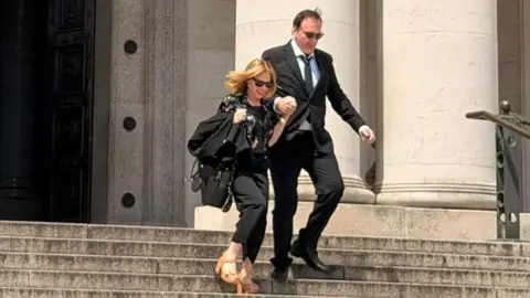 Amgueddfa Cymru – Museum Wales Quentin Tarantino and Kylie Minogue outside National Museum Cardiff. They are walking down the steps outside the museum holding hands. They are both wearing all black outfits and sunglasses. Kylie has a pair of brown tan high heels on.