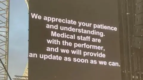 A sign with a black background and white lettering reads: We appreciate your understanding. Medical staff are with the performer, and we will provide an update as soon as we can.