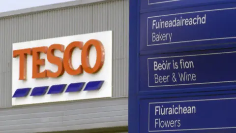 BBC Tesco in Stornoway with Tesco sign in background and a blue sign in the foreground