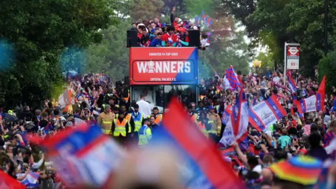PA Media Crystal Palace players on a open-top bus pass by fans during the FA Cup winners parade on 26 May 2025.