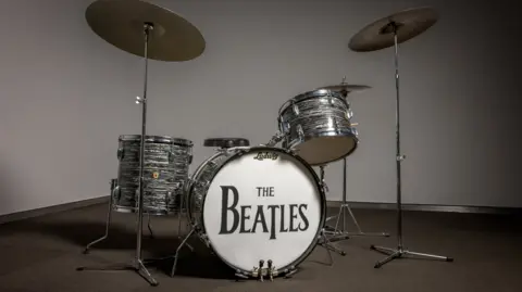 PA Media A drum kit standing on a grey carpet. 'The Beatles' is etched on the face of the bass drum in black letters. 