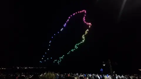 An outline of the Isle of Man in drone show colourful lights over a large crowd in Douglas