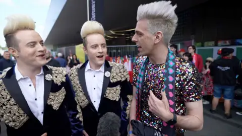Jedward laugh as they speak to a German man with a similar hairstyle.