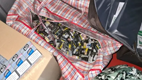 A large red and white checked laundry bag full off black packets of ilegal cigarettes