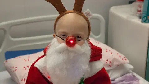 Gold Geese A girl in a hospital bed dressed in a red Santa costume and a plastic red nose reindeer bulb for a nose