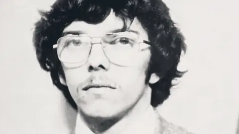 Cwmni Da/S4C A black-and-white headshot of Kenner Jones. He has black, slightly long hair with sideburns and a light moustache and wears wire-rimmed glasses.