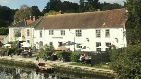 Phyllida Scrivens  Rushcutters pub in 2020, as pictured from rail bridge. People are sat outside, and a boat can be seen in the water