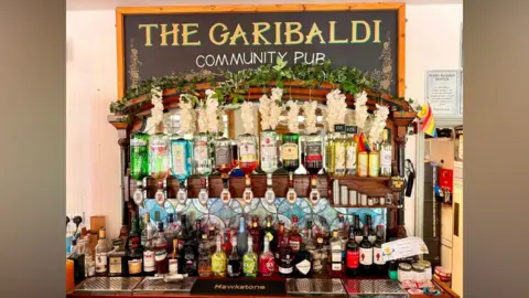 Supplied The behind of a bar. There are loads of bottles of spirits. 