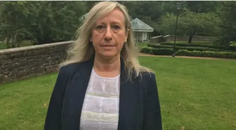 Anna-Louise Marsh-Rees in black jacket which is over a white lace top. She is stood in a garden and is looking at the camera.