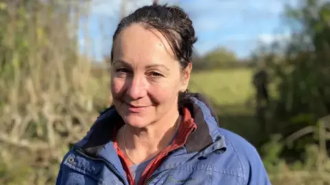 Catherine Withers. She has her hair tied back and is wearing a blue coat.