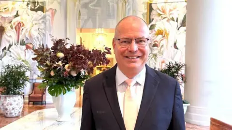 InterContinental Buckhead Atlanta Manuel Deisen, smiling, wearing a white shirt and dark suit jacket in a hotel lobby.