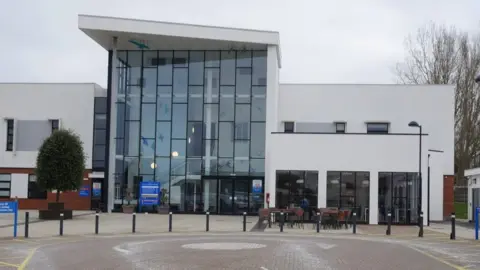 David Pashley/Geograph Exterior of Cromer Hospital. It has a large atrium area with dozens of windows and much of the building is painted white.